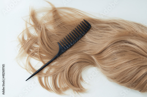 Long blond hair and black comb on white background.