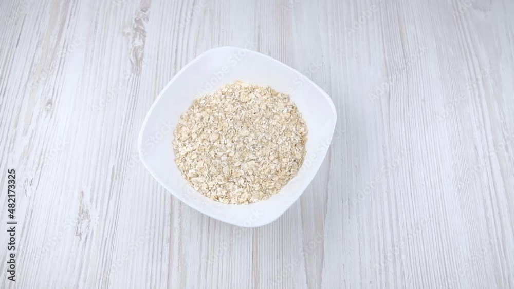 Oatmeal in a white plate. A woman's hand puts a plate on the table. Oatmeal recipe
