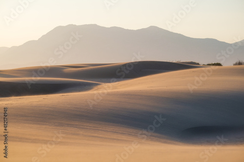 The sand dunes during sunset and strong wind. Summer landscape in the desert. Hot weather. Lines in the sand.
