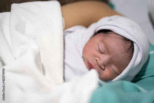 Cute infant Caucasian newborn baby which is sleeping on mother's embrace, baby portrait close-up photo.