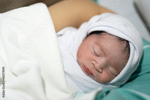 Cute infant Caucasian newborn baby which is sleeping on mother's embrace, baby portrait close-up photo. © Nattawit