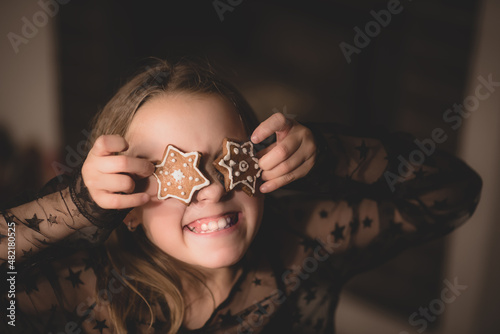A smiling girl holding gingerbread and covering her eyes 