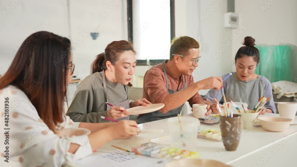 Group of Happy Asian man and woman friends enjoy and having fun indoor lifestyle painting self-made pottery together at pottery studio. Hobby leisure activity handmade ceramic art painting workshop. Group of Happy Asian man and woman friends enjoy and having fun indoor lifestyle painting self-made pottery together at pottery studio. Hobby leisure activity handmade ceramic art painting workshop.