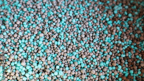 Mixed chemical fertilizer granules background. Abstract texture of primary mineral granules containing N  nitrogen   P  phosphorus  and K  potassium  for use in agricultural farms. Selective focus