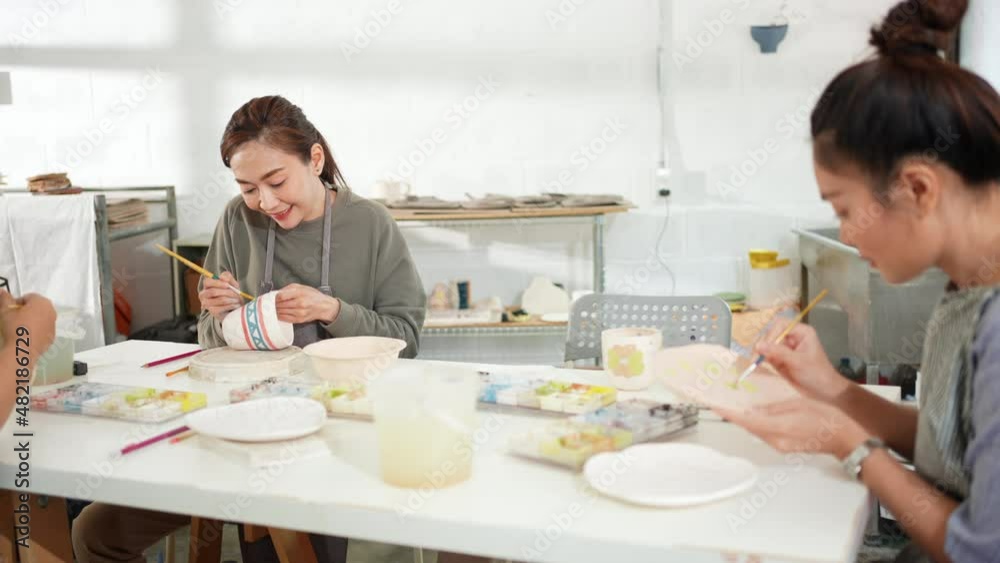 Asian woman learning color painting self-made pottery mug with friends at home. Confidence female enjoy leisure activity handicraft hobbies ceramic sculpture painting workshop at pottery studio. Asian woman learning color painting self-made pottery mug with friends at home. Confidence female enjoy leisure activity handicraft hobbies ceramic sculpture painting workshop at pottery studio.