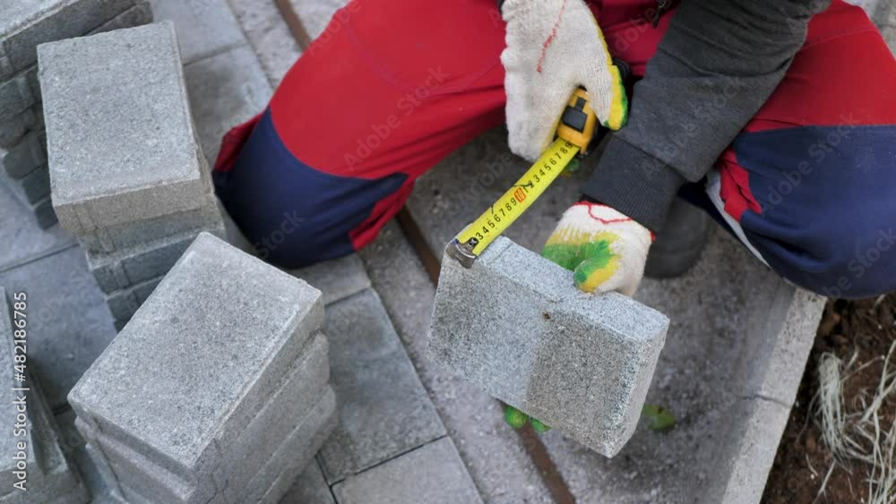 A builder measuring paving slabs with a centimeter tape measure. Stock