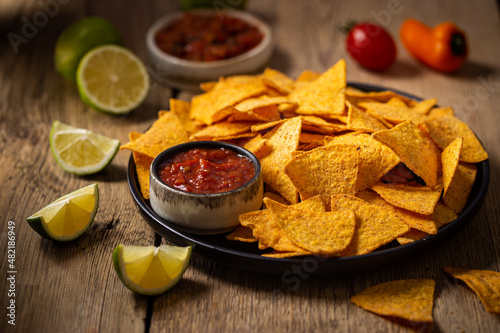 Single big black plate of yellow corn tortilla nachos chips with salsa sauce over wooden table photo