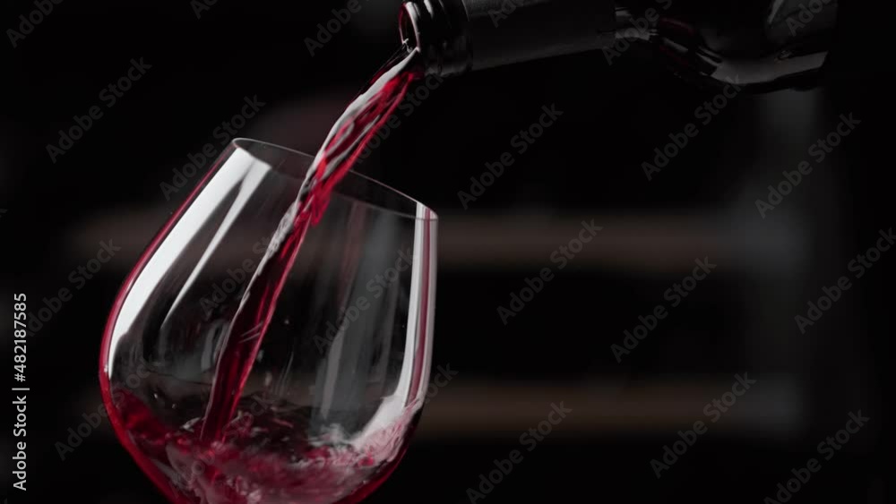 Pouring red wine to glass. Slow motion video.