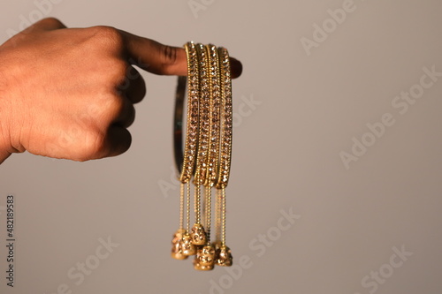 a girls finger holding a set of stone-studded bangles with tiny tassels hanging on it