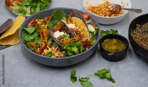 Vegan Mexican taco bowl consisting of corn, lentil, vegan cream, greens, pickles