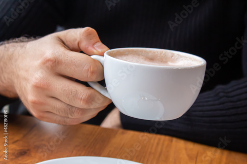 Man holding a cup of coffee white sitting in a cafe.