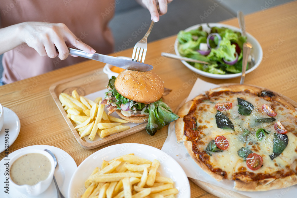 Close up of young woman eating hamburger and salad at restaurant with feeling happy and enjoy to eat. Italian food. Enjoy eating concept. Back view. Close up of young woman eating hamburger and salad at restaurant with feeling happy and enjoy to eat. Italian food. Enjoy eating concept. Back view.