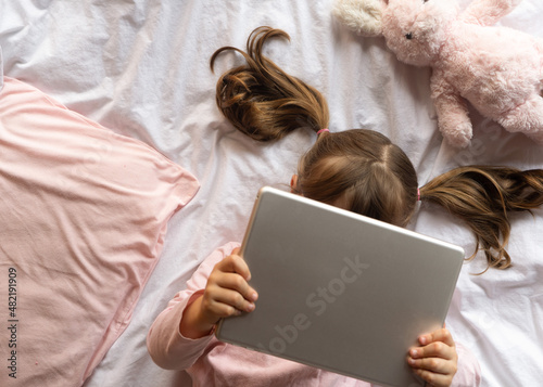 Little kid lying on bed using tablet, no face. 