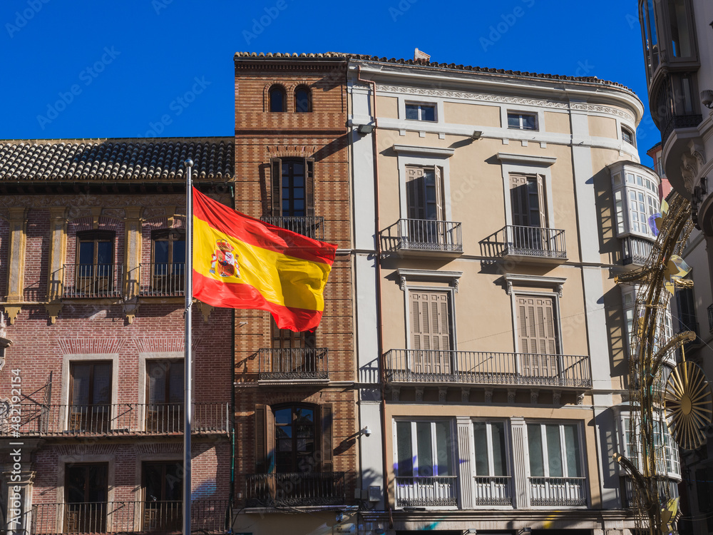 Flag of Spain fluttering in the wind in central street of Malaga, Marqués de Larios