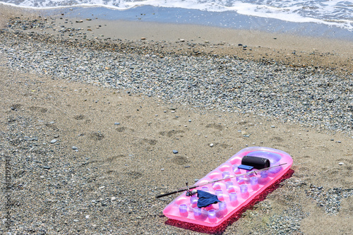 pink inflatable mattress on the beach among the rocks  a fishing rod and a column
