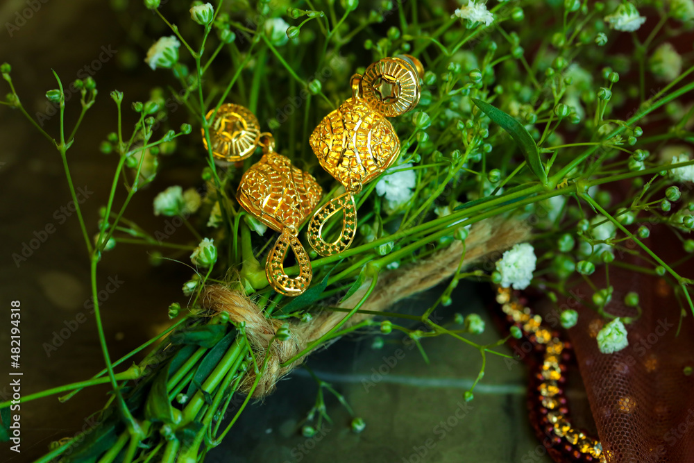a pair of intricate designer gold earrings with drops on a green flowery plant a pair of intricate designer gold earrings with drops on a green flowery plant