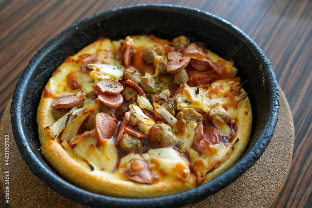 Barbeque beef pizza hut served on a black plate or bowl with a brown textured wooden table background. Barbeque beef pizza hut served on a black plate or bowl with a brown textured wooden table background.