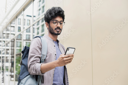 Handsome man using smartphone in a city. Smiling student men texting on his mobile phone. Young businessman with mobile phone in city. Modern lifestyle, connection, business concept