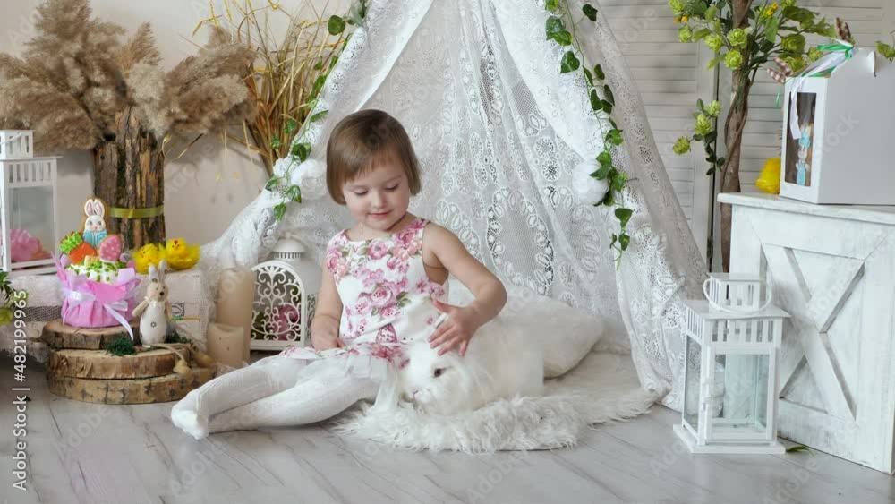 Little girl in a beautiful dress is ironing a cute white rabbit on Easter holiday. Little girl in a beautiful dress is ironing a cute white rabbit on Easter holiday.