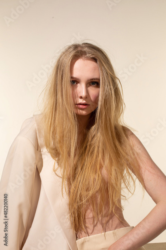 Young woman with blonde hair isolated on beige in light blazer