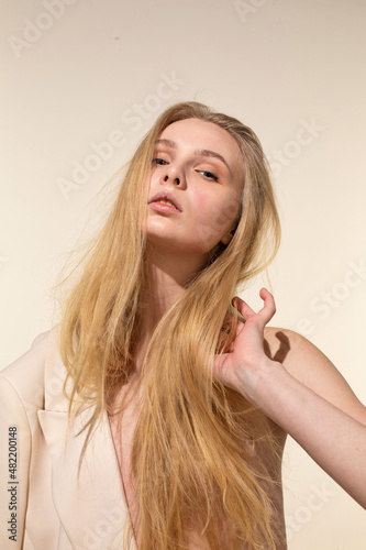 White young woman with blonde hair isolated on beige holding her hair by hand