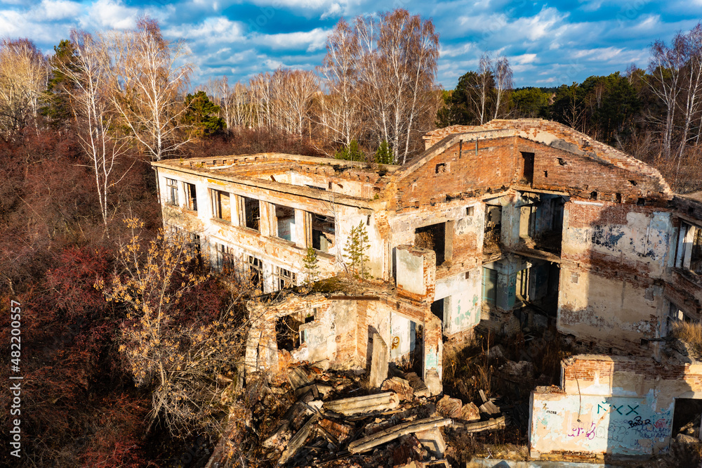 Remains of an abandoned burnt-out building with pipes in middle of green forest, a bird's-eye view from a drone.
