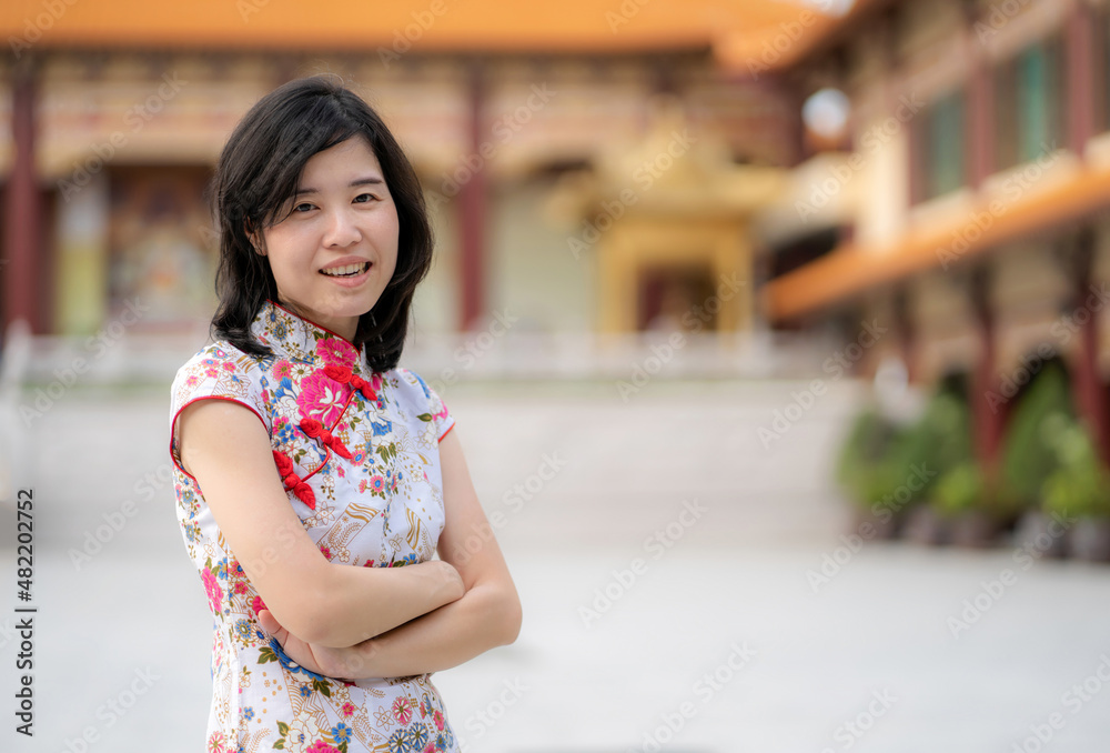 Confident Asia woman wearing Chinese traditional dress cheongsam or qipao standing in the temple with blur background. Feeling happy on Chinese lunar new year celebration with smile. Holiday concept