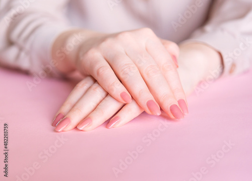 Female hands on a pink background. Beautiful well-groomed hands with classic manicure.