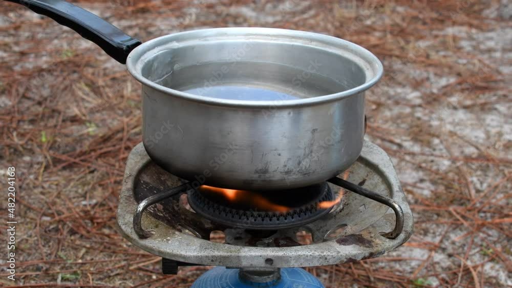 saucepan with water heated on a gas stove when camping: boiling water for cooking food in a container on a portable gas heater saucepan with water heated on a gas stove when camping: boiling water for cooking food in a container on a portable gas heater