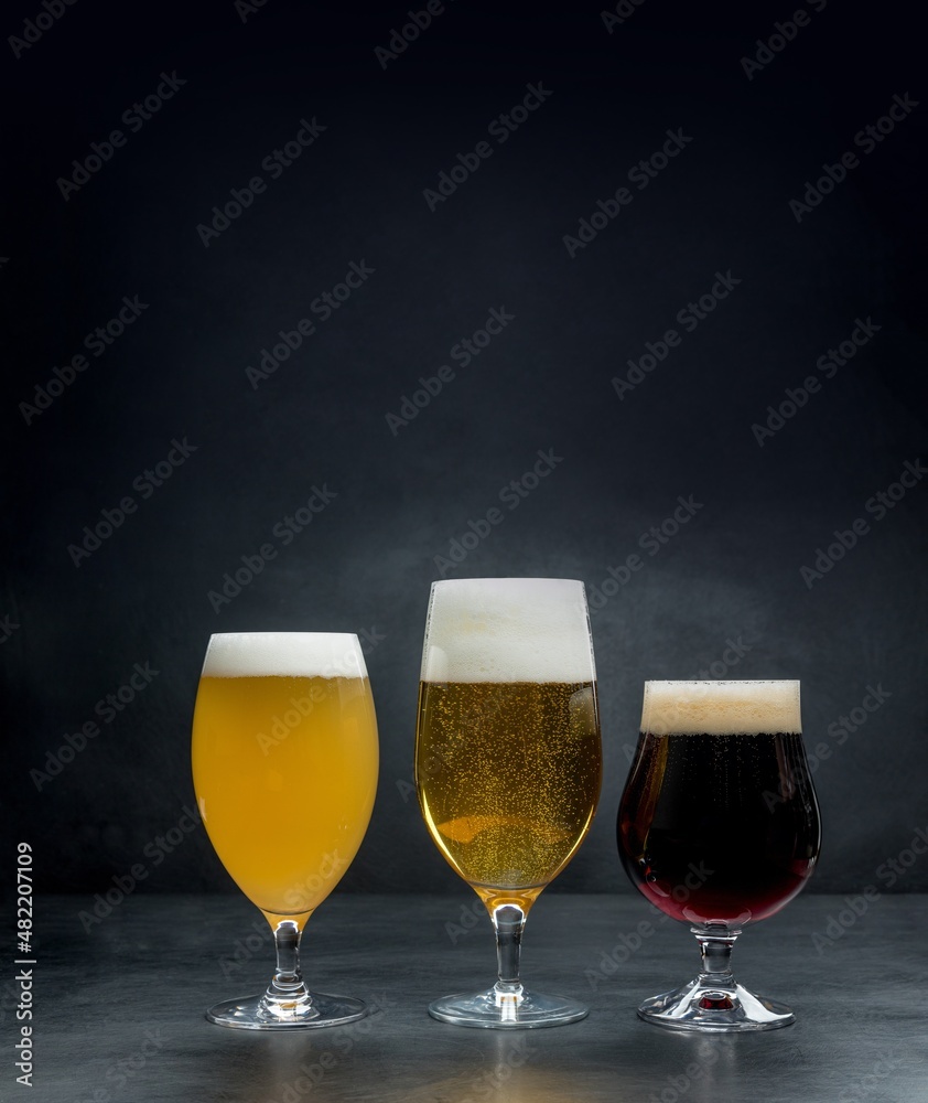 Three glass cups with different beers on a dark textural background.