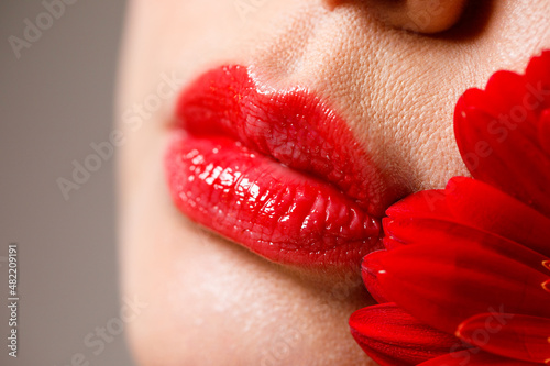 Sexy full female lips with red lipstick on the background of a flower. Aesthetic medicine services lip shape correction, lip augmentation.