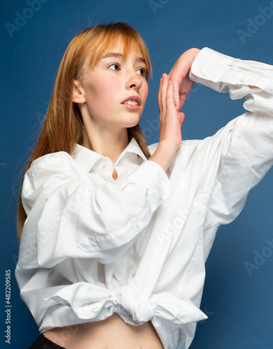 Girl with red hair and white skin isolated on blue in white shirt