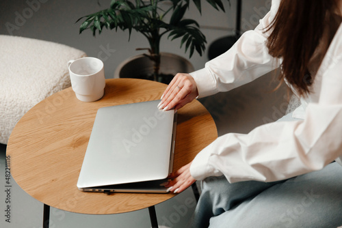 Young woman is closing her laptop. Young woman is sitting in a chair in a light background