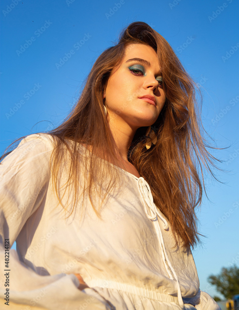 Young woman with white skin with sky behind with blue eyeshadow makeup