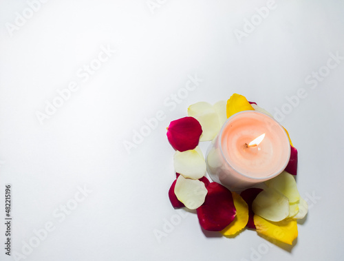 valentine's day decoration with scented candle and rose petals of red, yellow, white colors in white background.