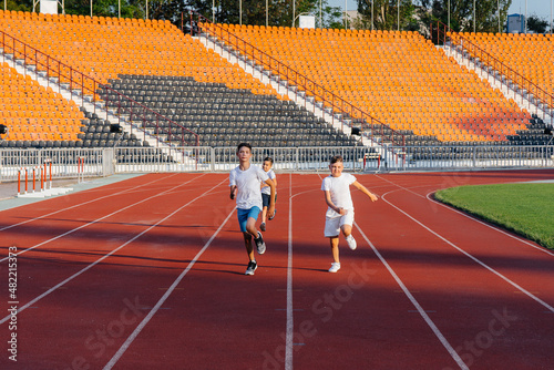 A large group of boys ' children are taught by a coach at the start before running at the stadium during sunset. A healthy lifestyle.