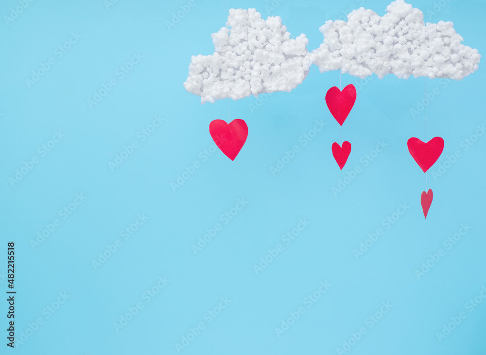 White clouds and red paper hearts in the form of rain on a blue background. 