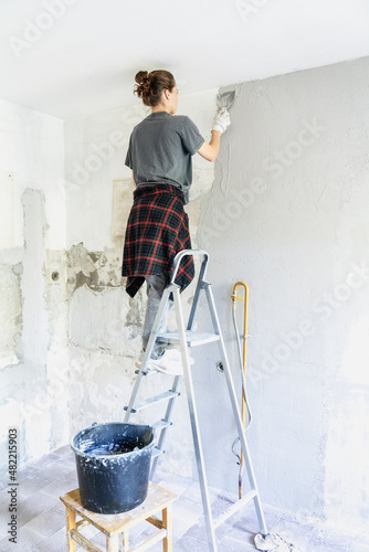 Young woman doing home repairs by applying plaster on the wall using a trowel, vertical shot
