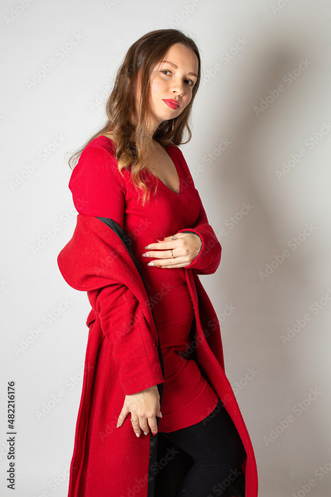 Fototapeta premium Attractive young european woman in red coat isolated on light grey