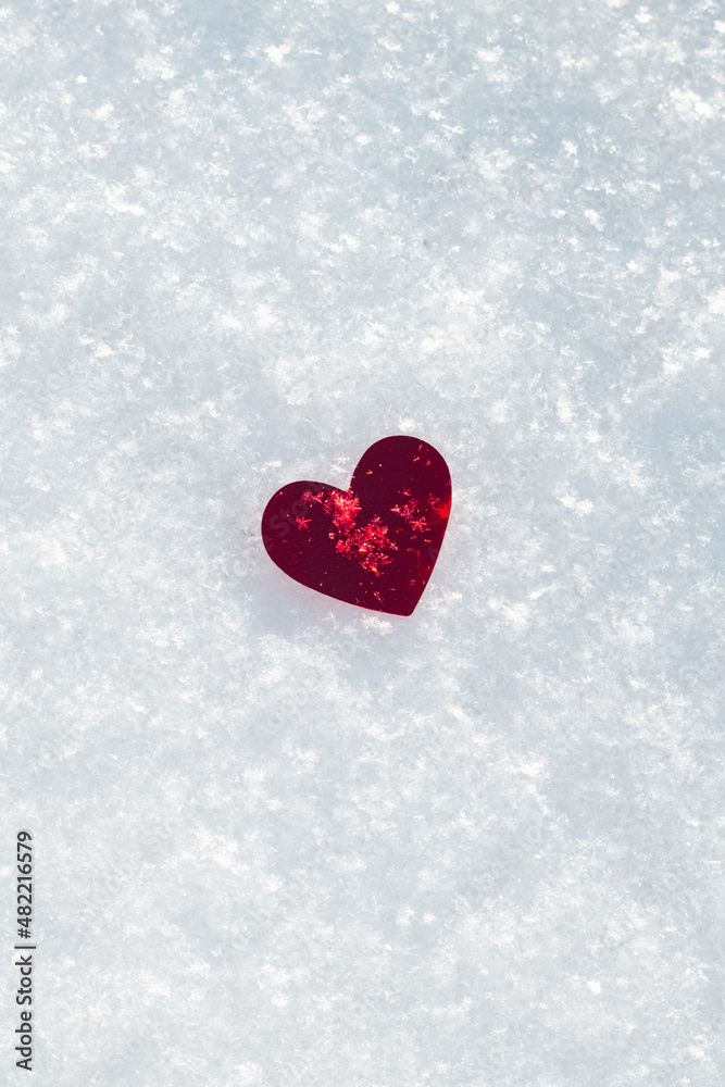 A red heart lies in the snow on a sunny day, a place for text
