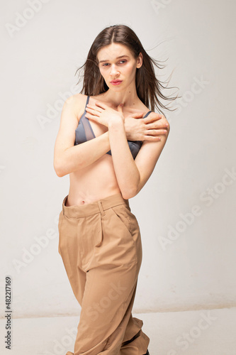 Young slim woman with dark straight hair isolated on beige with crossed arms on her chest
