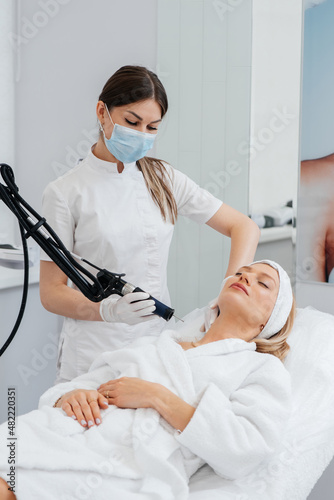 A young girl gets a carbon peeling for the skin of the neck in a beauty salon. Laser pulses cleanse the skin. Hardware cosmetology. The process of photothermolysis, warming the skin. © Andrii