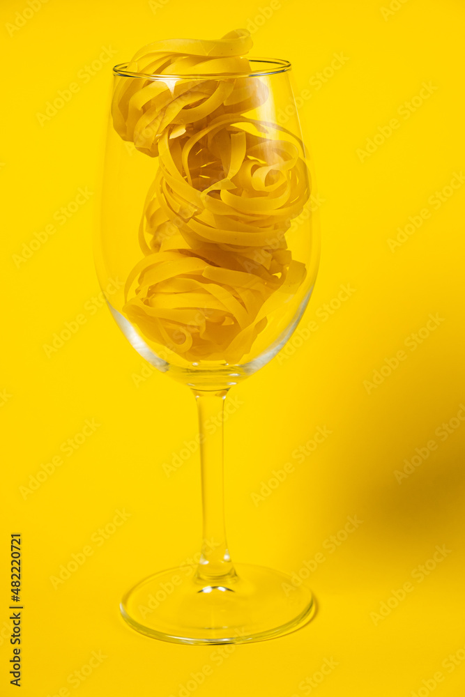 Raw fettuccine pasta in a wine glass isolated on yellow background