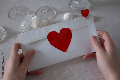 Foto a person's hands hold an envelope with a heart, a valentine, a declaration of love, against a background of cakes and candles