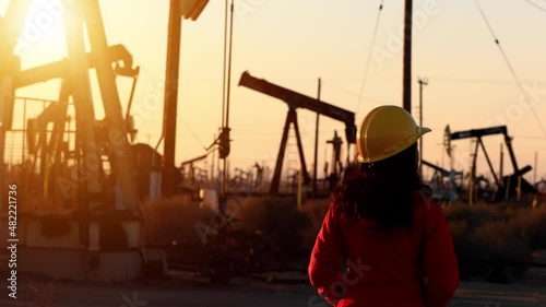 An Asian woman engineer inspects oil pumps at sunrise in a large oil field in California.