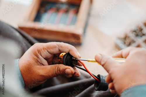 Closeup shot of hand of an Indian man fixing electronic item with screwdriver in his hand. Electrician fixes an electronic appliance. Repair background. 
