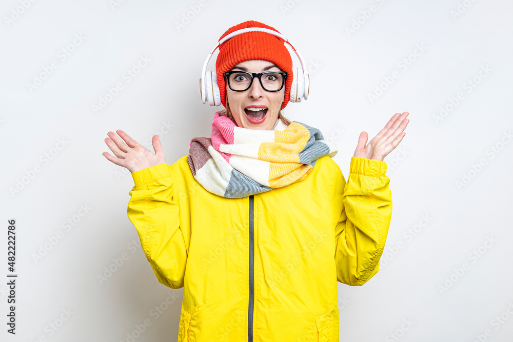 Cheerful surprised young girl in headphones, in a yellow jacket on a light background. Cheerful surprised young girl in headphones, in a yellow jacket on a light background.