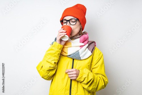 Beautiful young woman drinking coffee from a paper cup on a light background.
