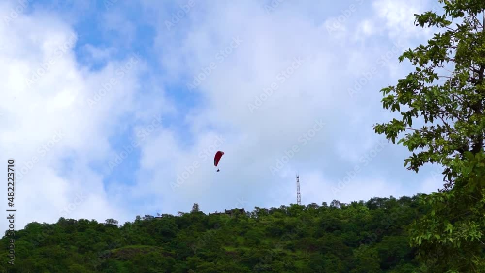 View of the tourists enjoying paragliding from above the hills at Saputara in Gujarat, India. Tourists experiencing Adventure activities at Saputara. Parachute in front of blue sky with clouds. View of the tourists enjoying paragliding from above the hills at Saputara in Gujarat, India. Tourists experiencing Adventure activities at Saputara. Parachute in front of blue sky with clouds.
