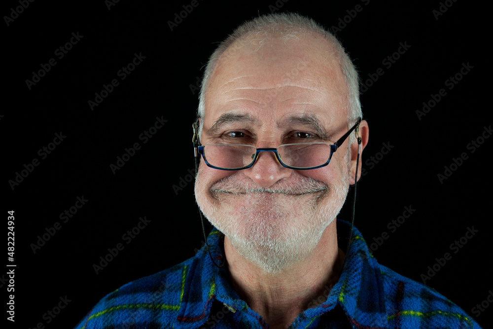 Old man with glasses grins mischievously at the camera against a black background. Old man with glasses grins mischievously at the camera against a black background.